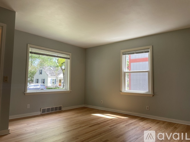 A room with two windows and wooden floors is available for rent.