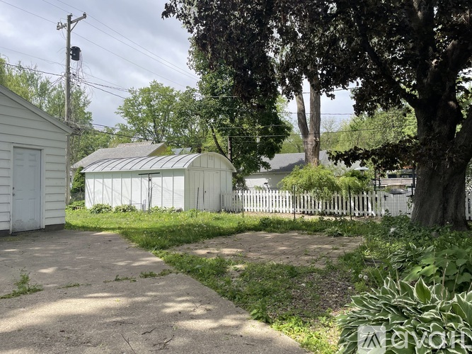 A white shed sits in a grassy area next to a white picket fence.