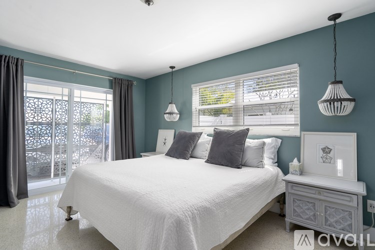 A bedroom with a large bed, a nightstand, and a window with blinds.