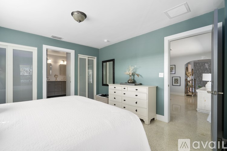 A bedroom with a white bed and a dresser with a mirror above it.