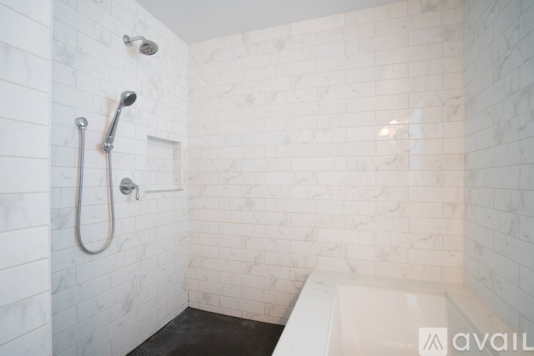 A white tiled shower with a black mat and a white bathtub.