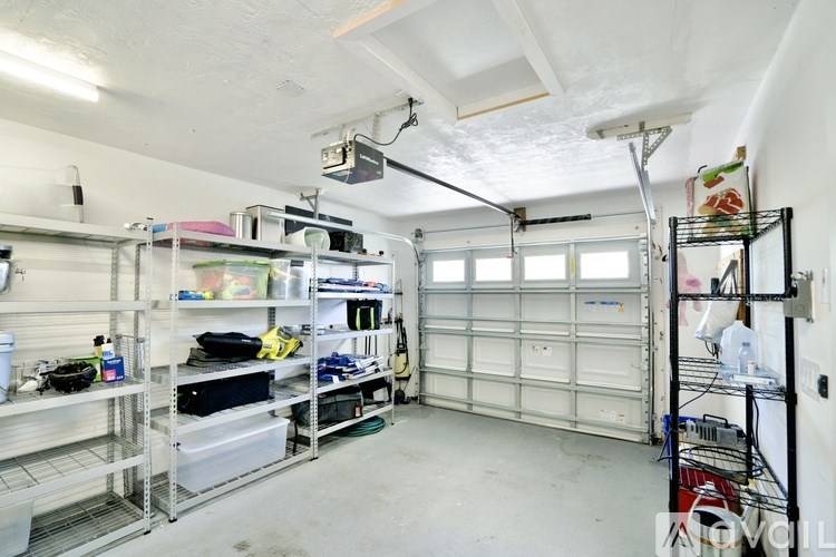 A garage with a white ceiling and walls, containing a variety of items on shelves and in storage containers.