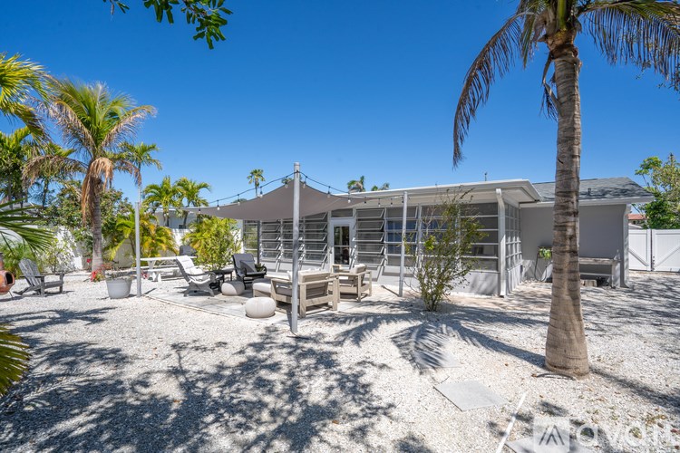 A sunny day at a beachfront property with a white building, palm trees, and beach chairs.