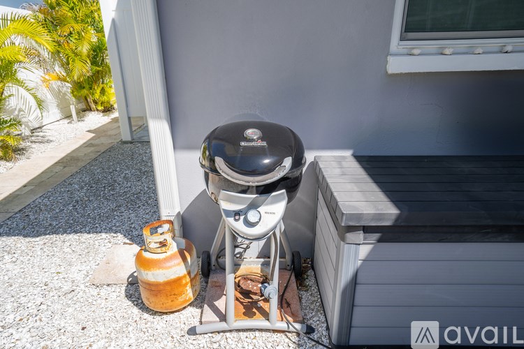 A black and silver grill is on a gravel surface next to a grill box.