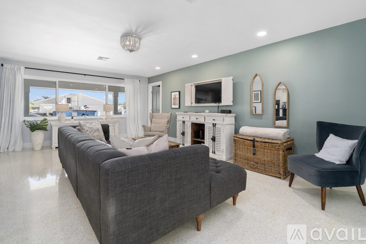 A living room with a grey sofa, a grey armchair, a white fireplace, and a large window with a view of the outside.