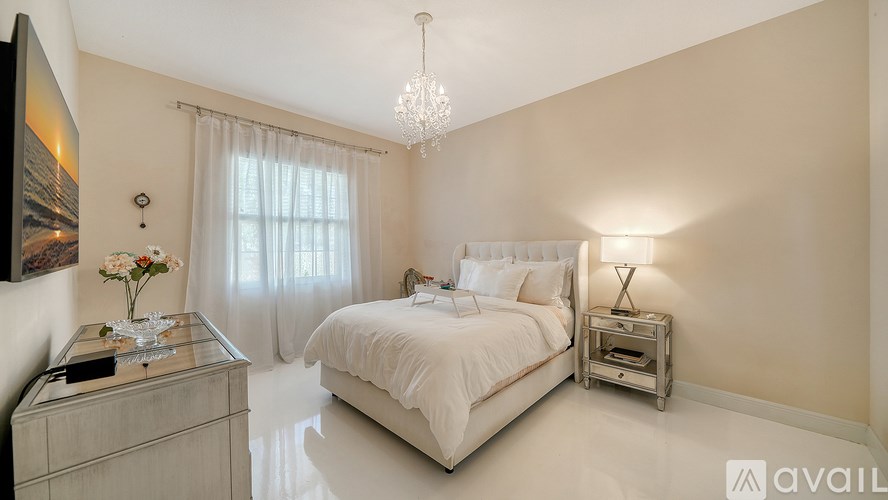 A bedroom with a large bed, a chandelier, and a dresser with a vase of flowers on top.