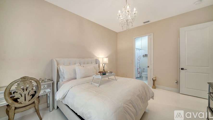 A bedroom with a large bed, a chair, and a chandelier.
