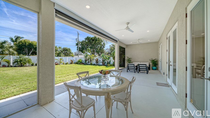 A patio with a glass table and chairs is shown with a view of a garden and a house.