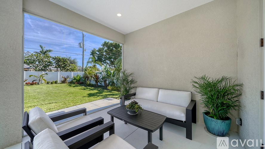 A patio with a white couch, black chairs, and a table with a plant on it.
