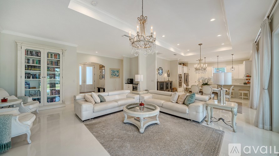 A spacious living room with white furniture and a chandelier.