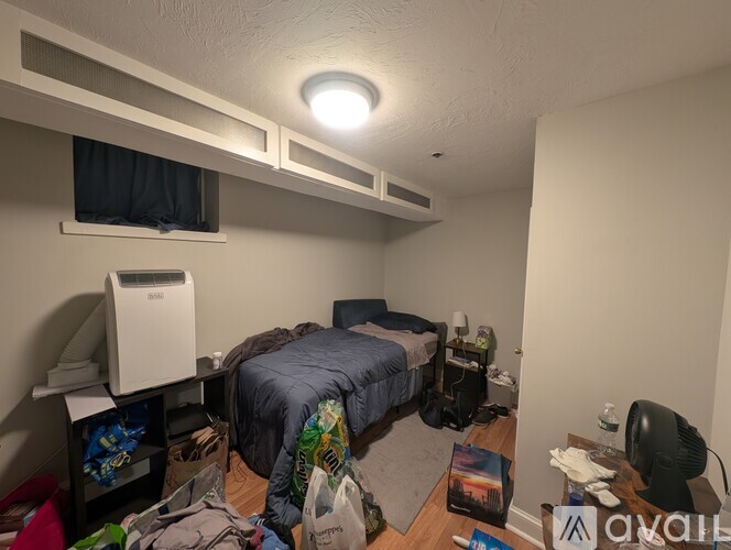 A small, messy bedroom with a bed, desk, and clutter on the floor.