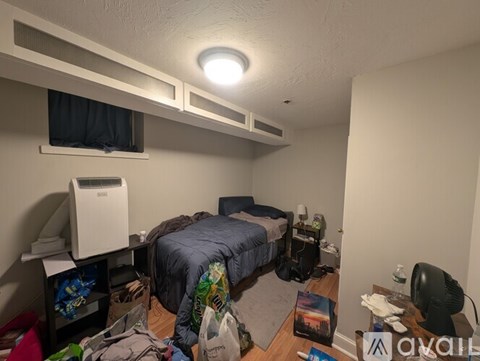 A small, messy bedroom with a bed, desk, and clutter on the floor.