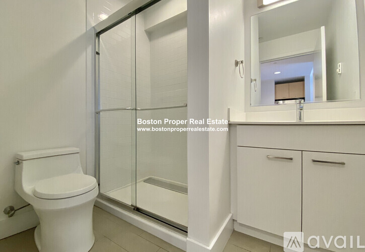 A white toilet in a bathroom with a glass shower door and a mirror above a cabinet.