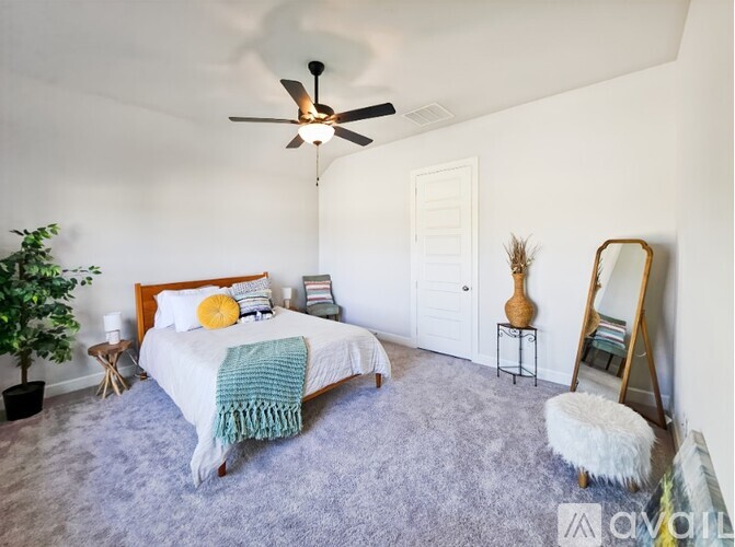 A bedroom with a bed, a chair, a plant, and a mirror.