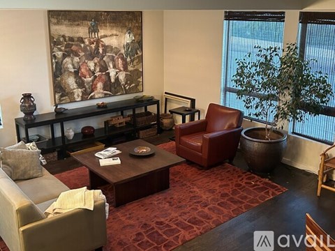 A living room with a large painting on the wall and a red rug on the floor.