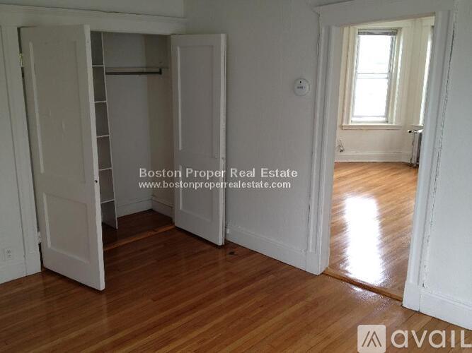 A room with wooden floors and white walls, with a door open to another room.