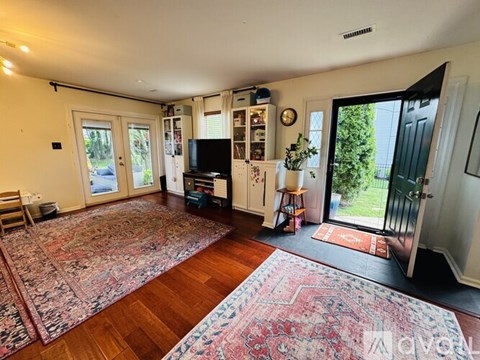 A living room with a rug on the floor and a television on the wall.