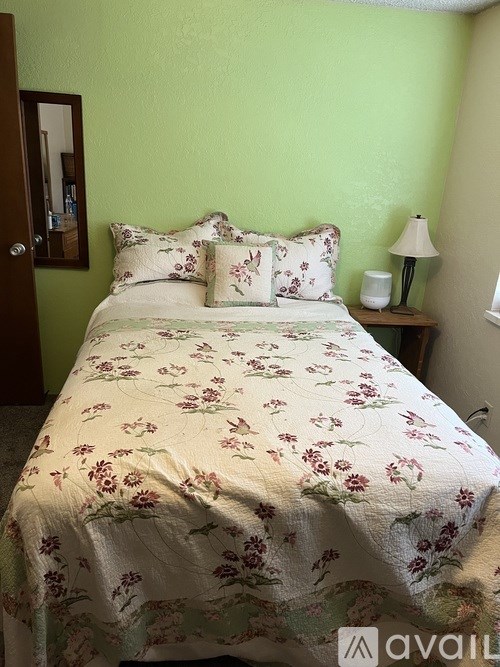A bed with a floral comforter and matching pillow cases sits in a room with green walls.