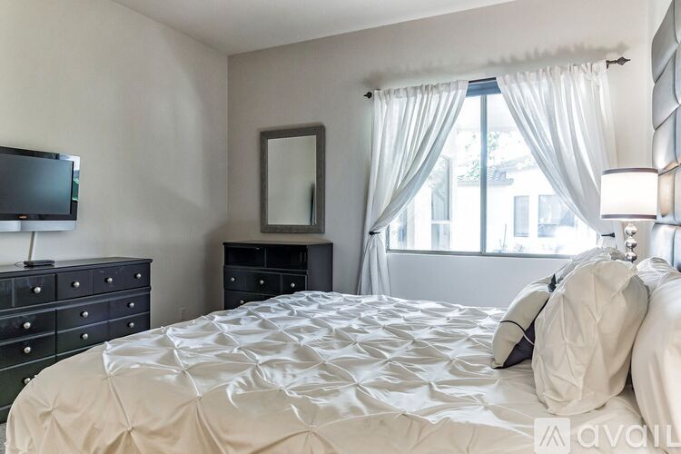 A bedroom with a large bed, a television, and a window with curtains.