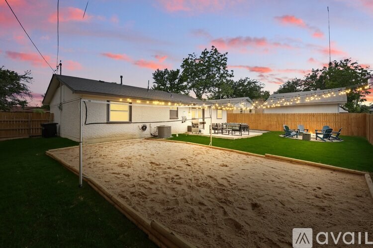A backyard with a sandbox and a house with lights on.