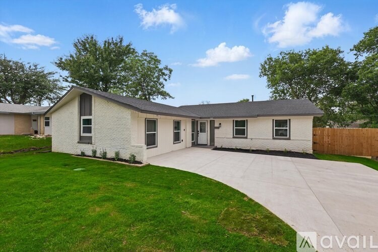 A house with a white exterior and a grey roof is surrounded by a green lawn and a wooden fence.