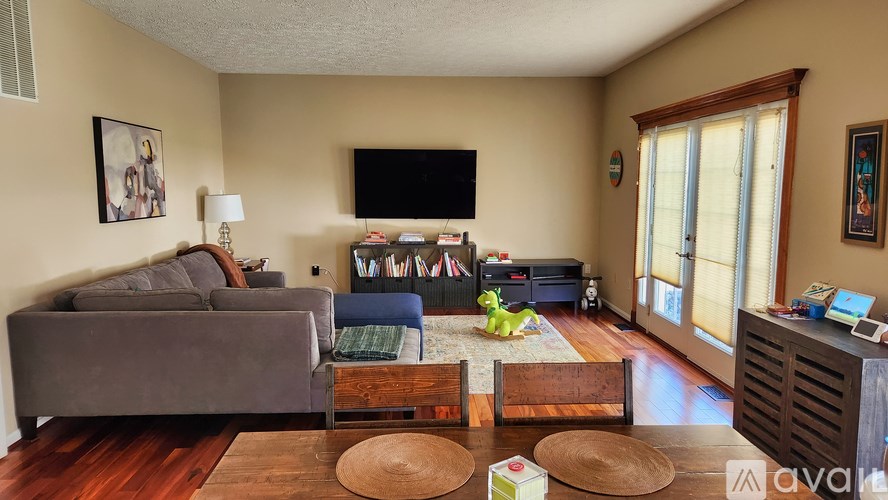 A living room with a grey couch, a blue ottoman, and a television on the wall.