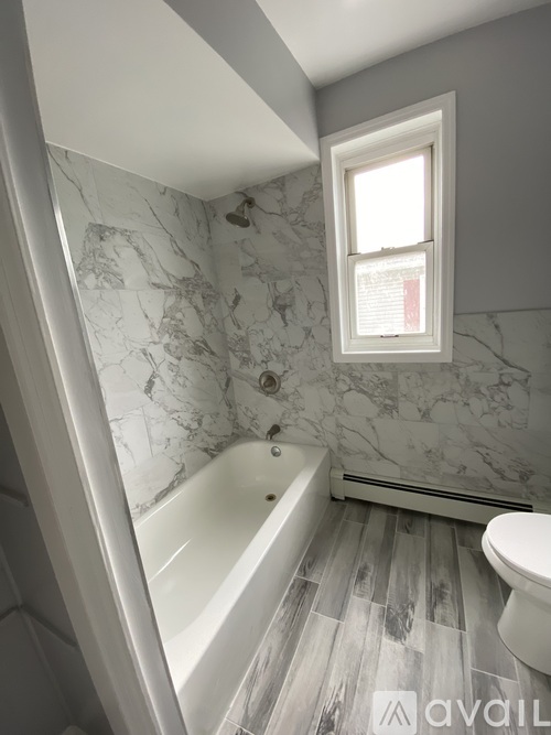 A bathroom with a marble patterned wall and a white tub.
