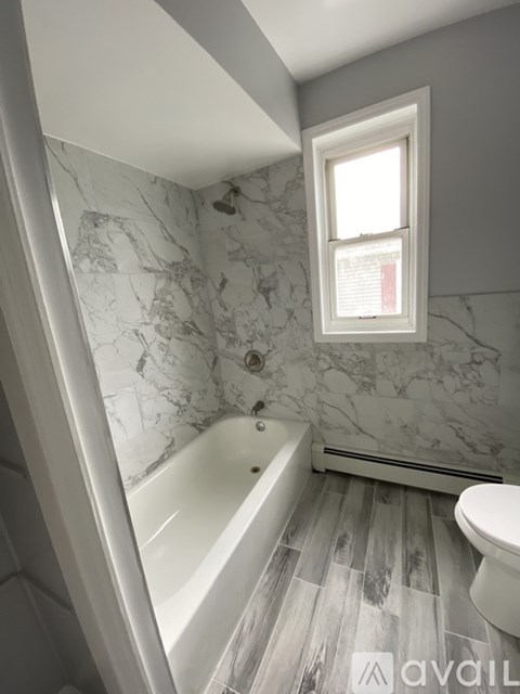 A bathroom with a marble patterned wall and a white tub.