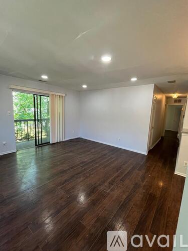 A spacious room with wooden flooring and a sliding glass door leading to a balcony.