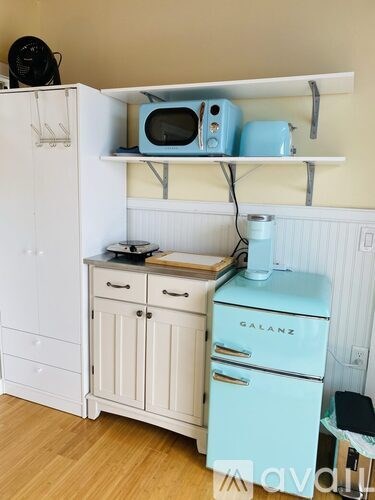 A kitchen with a white refrigerator, a blue toaster, and a blue microwave on a shelf.