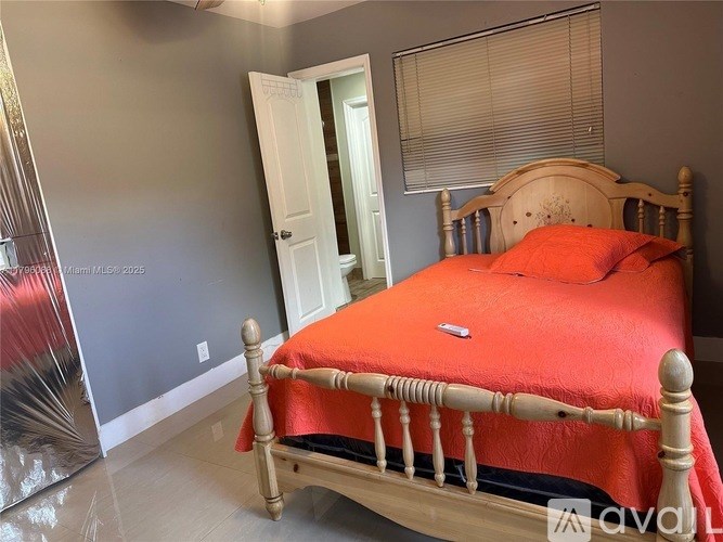 A bed with a red cover sits in a room with a wooden headboard.