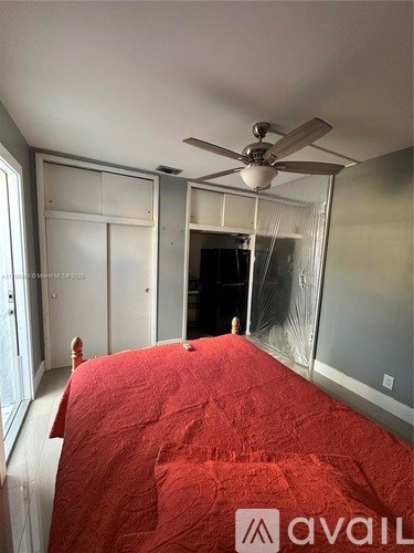 A bedroom with a red bedspread and a ceiling fan.