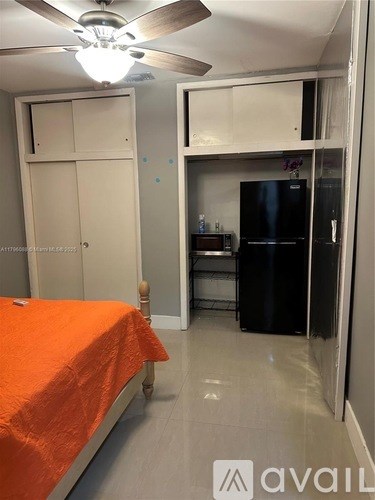 A bedroom with an orange bedspread and a black fridge in the kitchen area.