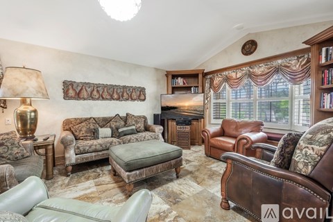 A living room with a brown leather couch and a green ottoman.