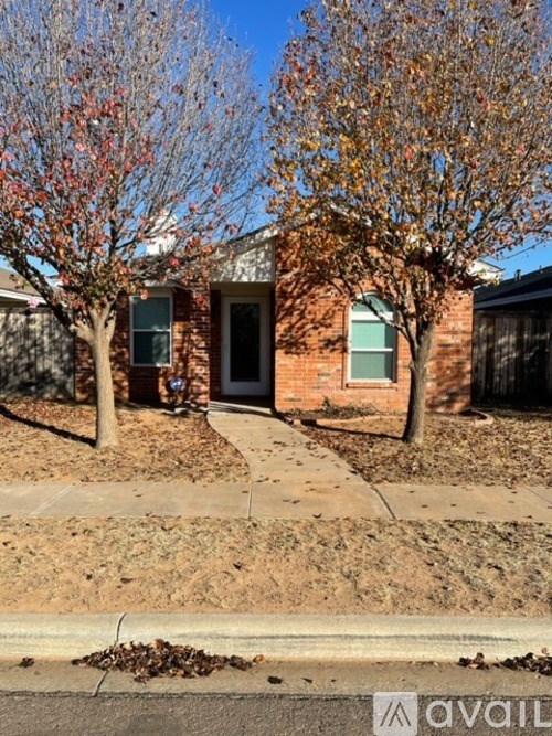 A house with a brick facade and a tree with red leaves in front.