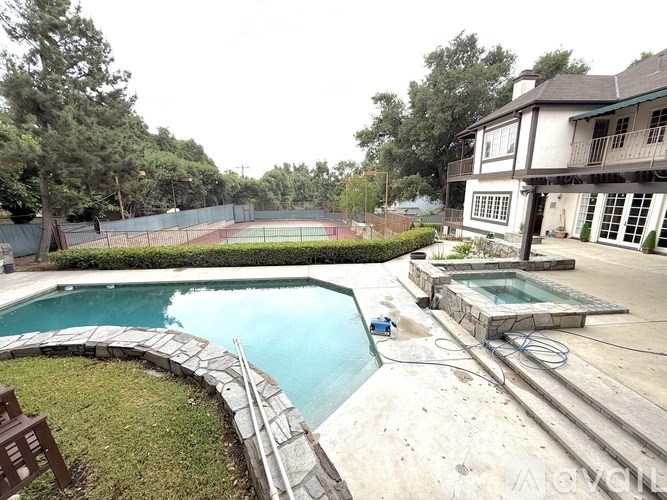 A swimming pool with a stone border and a hot tub in the middle of a backyard.