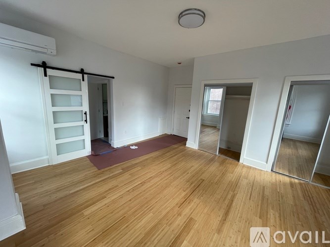 A room with wooden floors and white walls, with a door leading to another room.