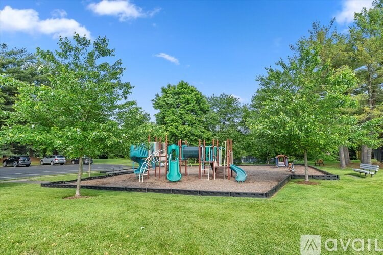A playground with a green slide and swings surrounded by trees.