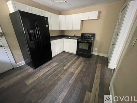 A kitchen with a black fridge, black oven and wooden floors.