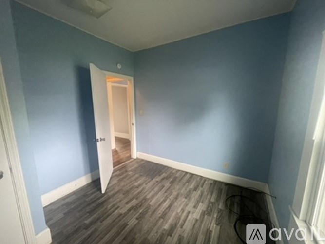 A room with blue walls and wooden flooring with a doorway leading to another room.