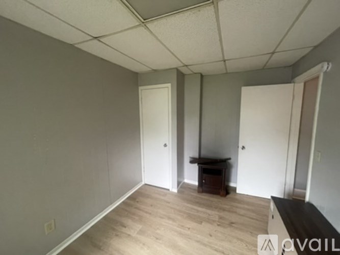 A room with a wooden floor and white walls, with a table and two doors.