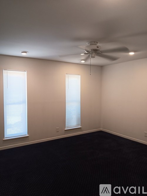 A room with a ceiling fan and two windows.