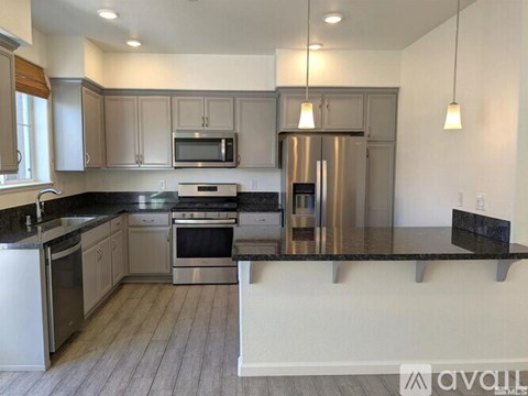 A kitchen with a stainless steel refrigerator and black countertops.