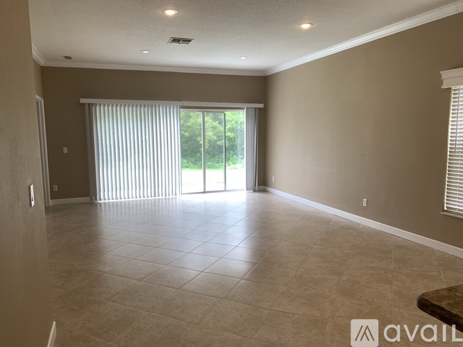 A spacious room with tiled flooring and a sliding glass door leading to a green outdoor area.