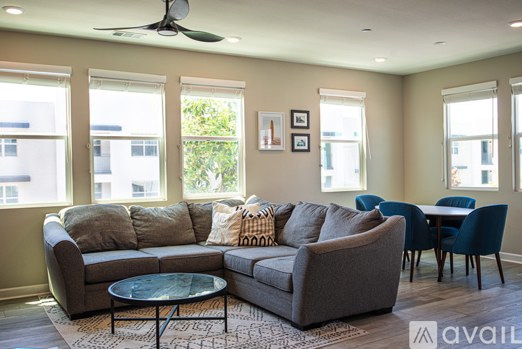 A living room with a grey couch, a glass table, and a ceiling fan.