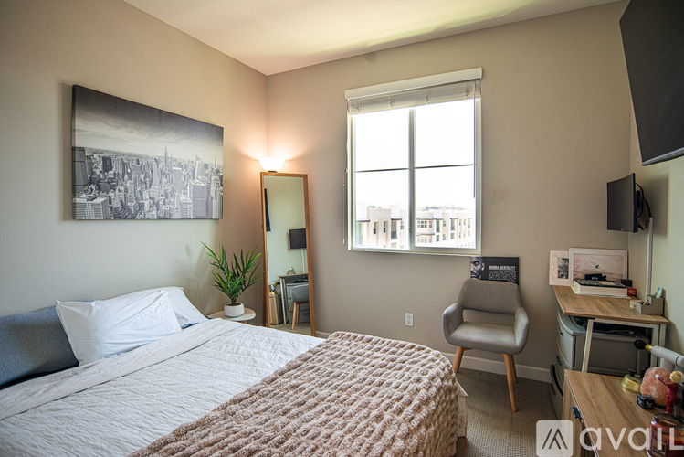 A bedroom with a bed, desk, chair, and a window overlooking the city.