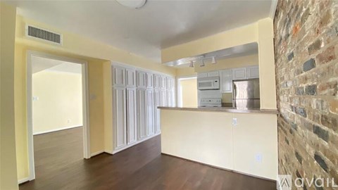 A room with a brick wall on the right side and a kitchen area with white cabinets and appliances.