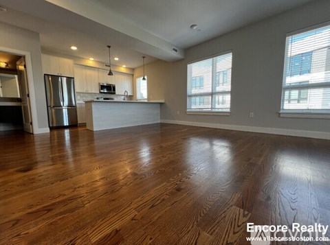 A spacious kitchen with wood flooring and a refrigerator.