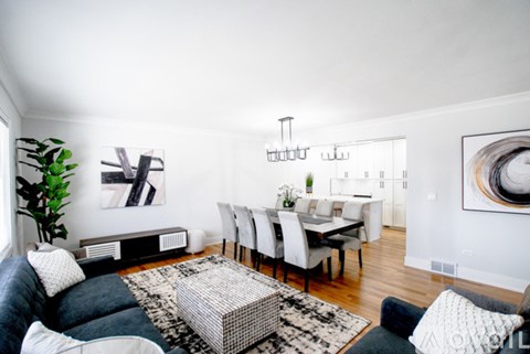 A modern living room with a black and white patterned rug, a black leather couch, a wooden dining table with white chairs, and a large abstract painting on the wall.