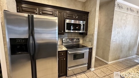 A stainless steel refrigerator stands in a kitchen with dark wood cabinets.
